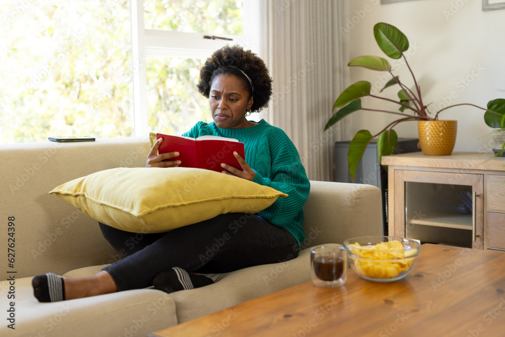 Plus size african american woman sitting on sofa and reading book at home Plus size african american woman sitting on sofa and reading book at home