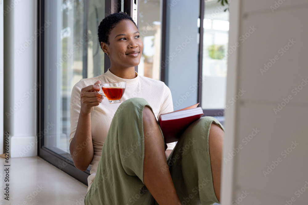 Happy african american woman sitting on floor, drinking tea and reading book Happy african american woman sitting on floor, drinking tea and reading book