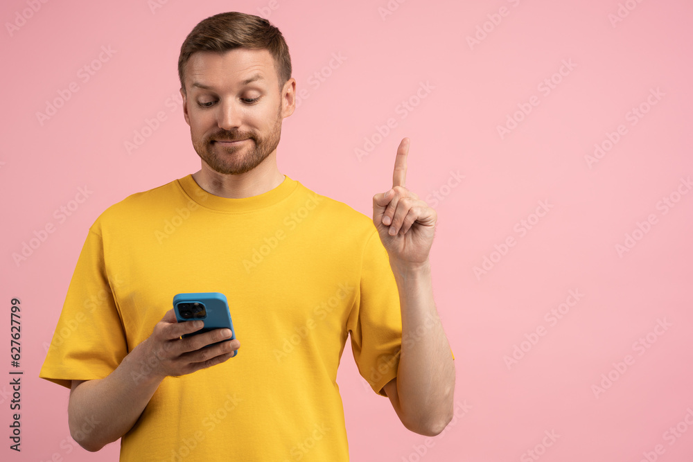 Interested man looking to smartphone screen having insight point finger up isolated on pink studio wall. Eureka. Pleased guy found necessary information in mobile phone posing on background copy space Interested man looking to smartphone screen having insight point finger up isolated on pink studio wall. Eureka. Pleased guy found necessary information in mobile phone posing on background copy space
