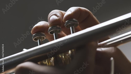 Slow motion video close up of musicians fingers pressing down on piston trumpet valves on a gray background