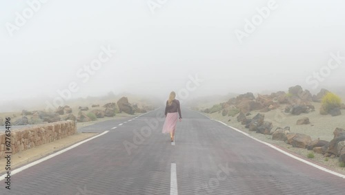 Girl in summer pink skirt walking on road, disappearing in mysterious fog