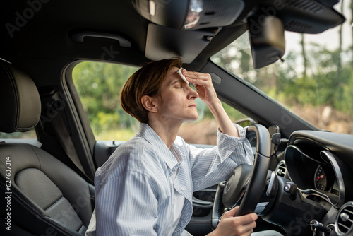 Woman drives car with broken air conditioning in hot summer weather. Wipes sweat paper napkin. Middle aged female suffering from heat stuffiness, high temperature, humidity. Overheated worried driver. © DimaBerlin