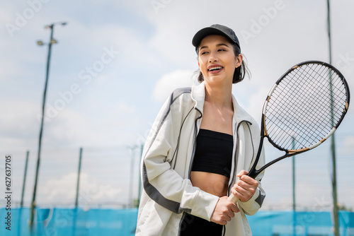 happy woman in active wear and cap holding tennis racket on court, female tennis player, motivation photo