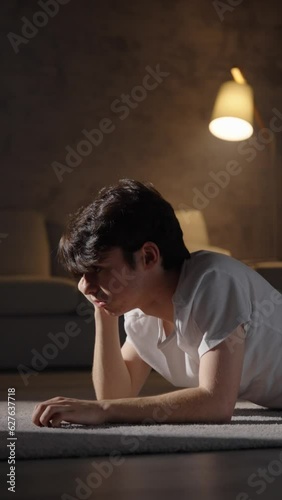 Sad teenager boy thinking at night lying on the floor. Depression, loneliness and adolescence problems concept.