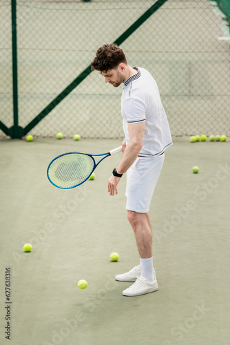 tennis balls around sportsman with racket on court, hobby and recreation, handsome player