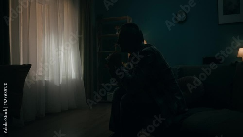 A devastated lonely young man sits in a room in the dark, going through a crisis. The man thinks, does not find a solution, hides his head in his palms. Transience of time, hopelessness. Slow motion.