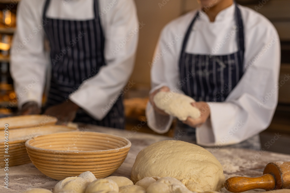 Diverse bakers wearing aprons in bakery kitchen and holding dough Diverse bakers wearing aprons in bakery kitchen and holding dough