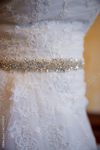 The details close up a of a white wedding dress. Sparkling belt with rocks and white embroidered flowers. High quality photo