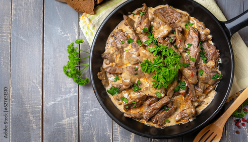 delicious beef stroganoff - veal strips stewed with porcini in sour cream sauce sprinkled with finely chopped parsley on skillet, authentic recipe, view from above