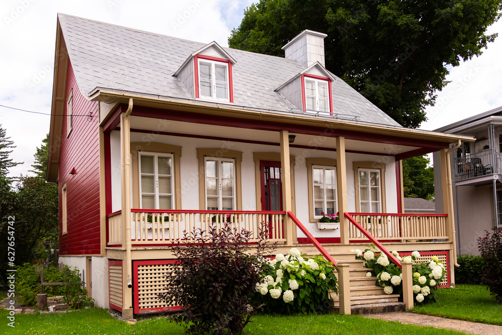 Obraz premium Pretty ancestral neoclassical house with metal sheet roof and red details in the Beauport area, Quebec City, Quebec, Canada