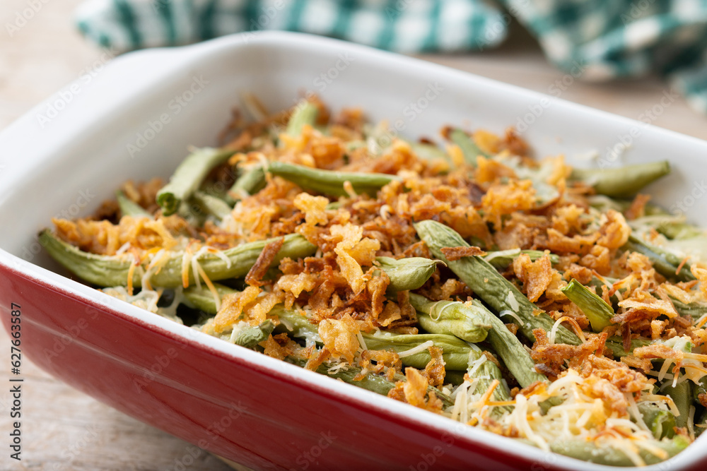 A traditional green bean casserole topped with French Fried Onions and cream of mushroom on wooden table