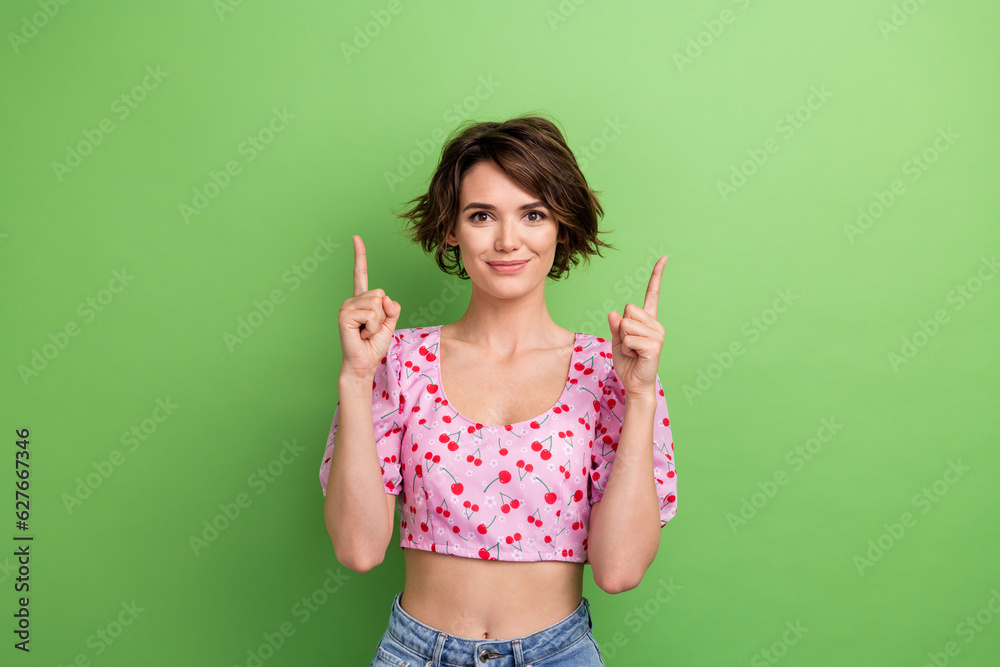 Photo of attractive young woman fingers point up empty space dressed stylish pink cherry print clothes isolated on green color background Photo of attractive young woman fingers point up empty space dressed stylish pink cherry print clothes isolated on green color background