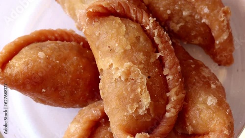 Indian festival sweet Gujiya or Gujia on small bowl isolated on white background. Table top spin view photo