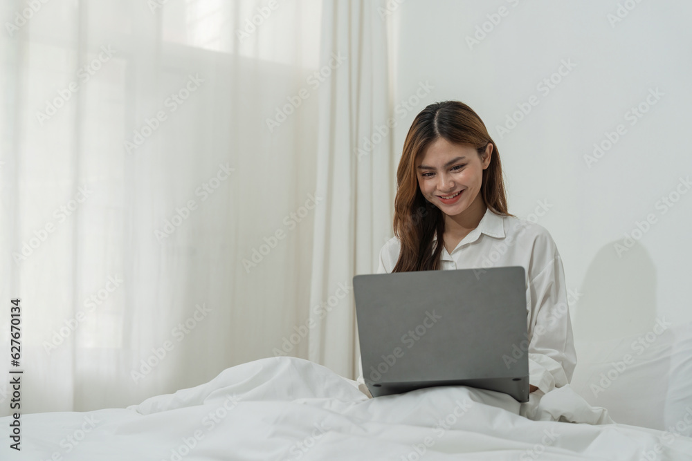 Beautiful happy asian woman lying in bed relaxed and looking at laptop screen. Girl smiling happy while browsing internet on computer, resting at home Beautiful happy asian woman lying in bed relaxed and looking at laptop screen. Girl smiling happy while browsing internet on computer, resting at home