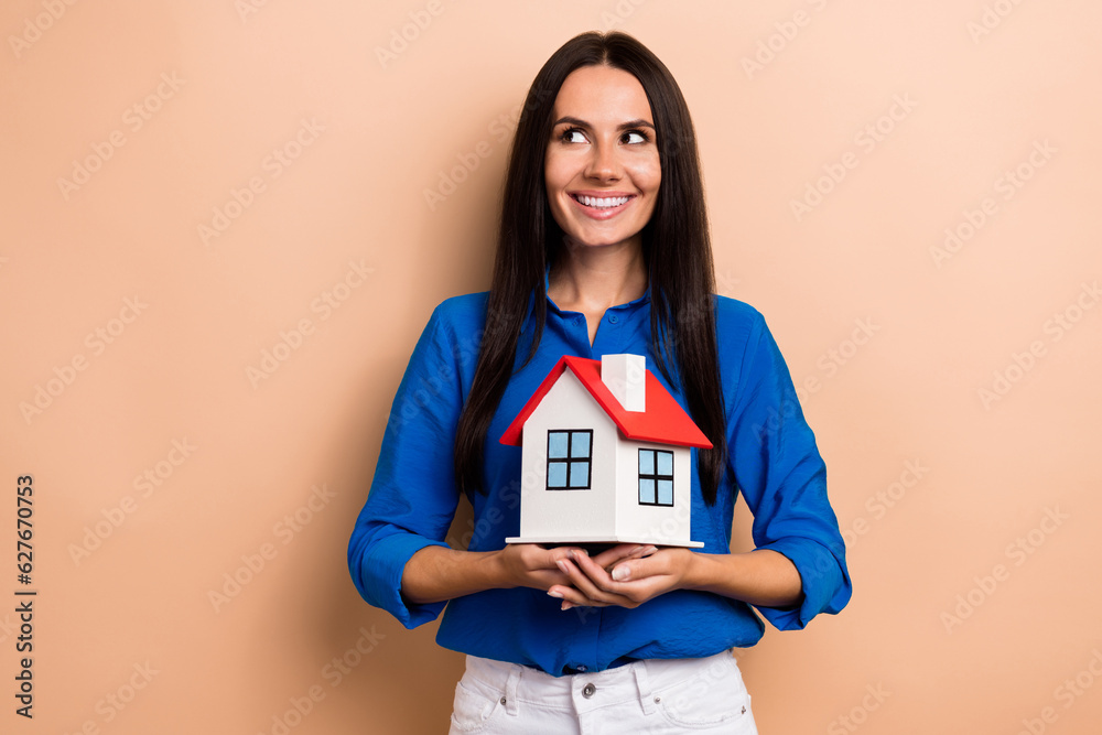 Photo of charming lady wear blue stylish clothes hand hold house look up empty space promo banner isolated on beige color background Photo of charming lady wear blue stylish clothes hand hold house look up empty space promo banner isolated on beige color background