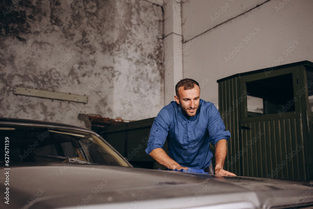 a man wipes dust from a retro car in the garage a man wipes dust from a retro car in the garage