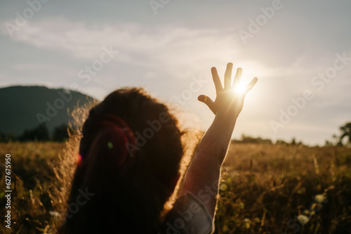 Silhouette of preteen girl kid raises his hand up on mountains background during amazing sunset or sunrise. Child enjoys an active weekend on summer day. Concept travel, childhood, adventure