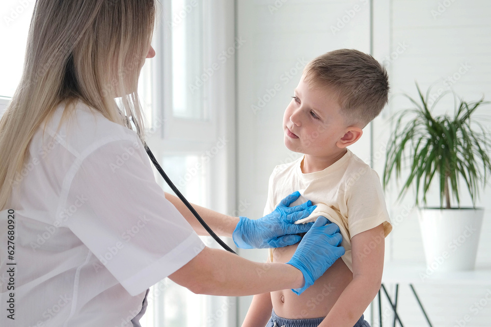 Fototapeta premium The doctor listens to the breathing of a little boy through a stethoscope. Pediatrician with stethoscope listens to the lungs of a child with bronchitis and cough