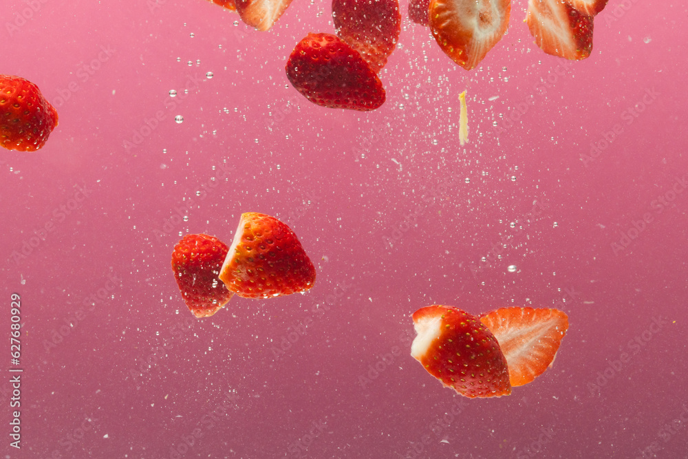 Fototapeta premium Close up of strawberries falling into water with copy space on pink background