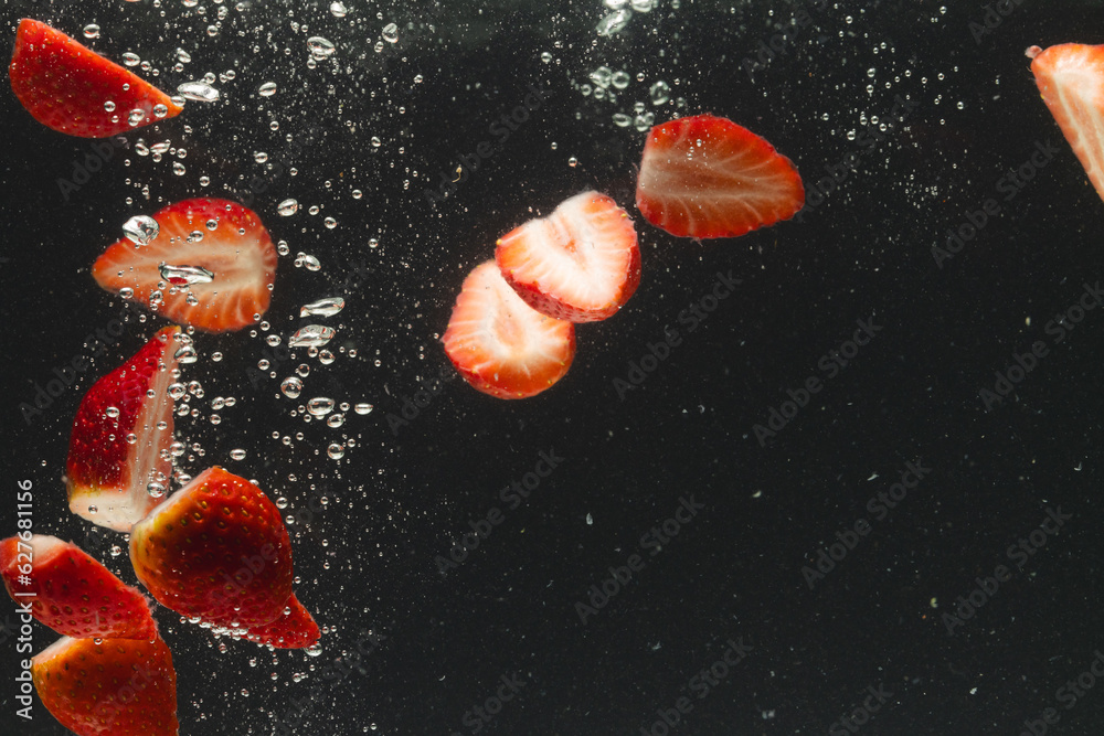 Fototapeta premium Close up of strawberries falling into water with copy space on black background