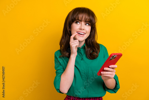 Photo of shiny excited girl dressed green shirt typing modern gadget looking empty space isolated yellow color background