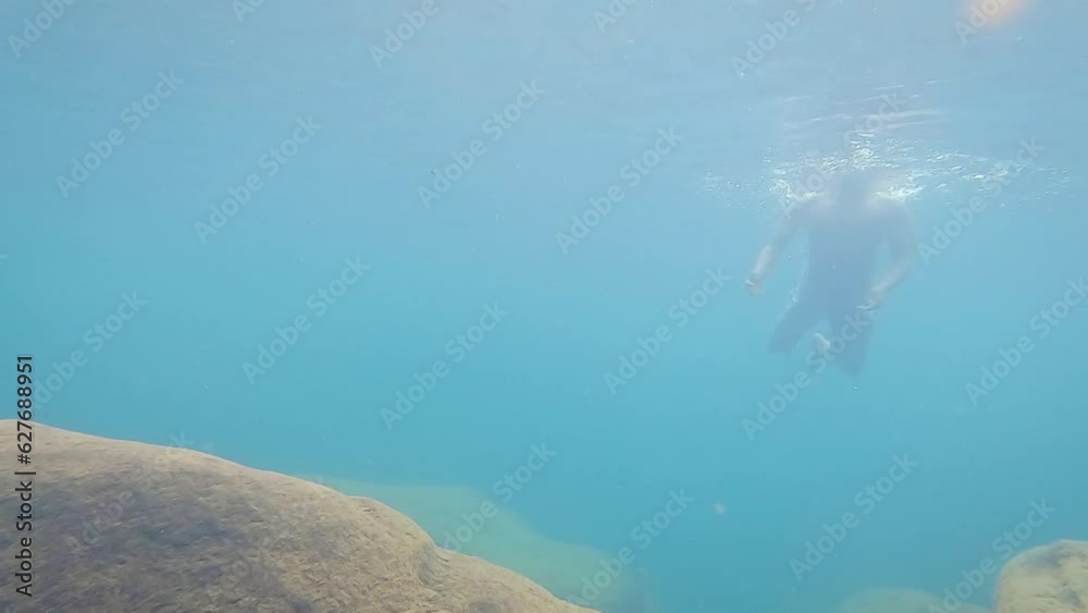 young man swimming underwater in clear blue water at day from low angle