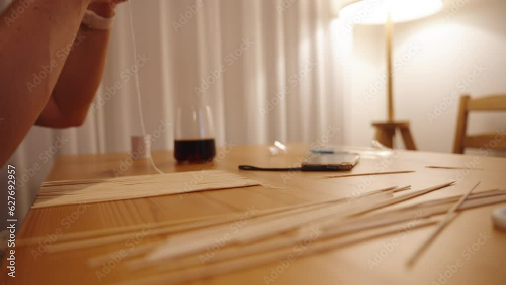 A woman is making a mat for rolling sushi using wooden skewers.