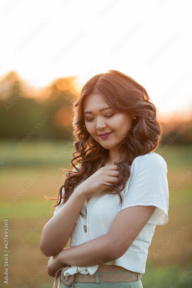 Beautiful young Asian woman in field at sunset. Model with dark long curly hair. Summer, sun.