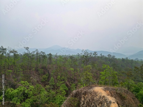 A forest at Pai Canyon in Pai in Thailand taken from above with the drone in the background hills with a smoggy sky.