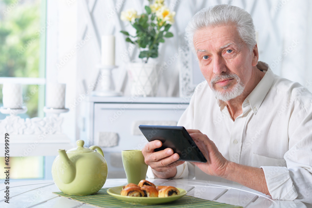 senior man using tablet while drinking tea senior man using tablet while drinking tea