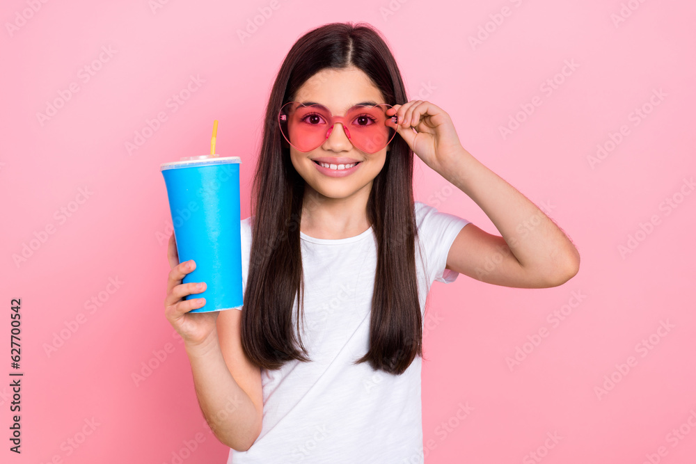 Photo portrait of pretty young child girl hold plastic cup drinking soda dressed stylish white clothes isolated on pink color background Photo portrait of pretty young child girl hold plastic cup drinking soda dressed stylish white clothes isolated on pink color background