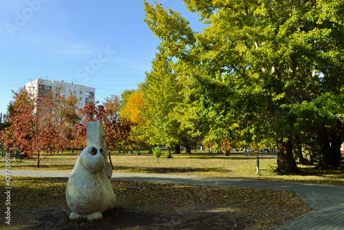 The sculpture of the strange creature and the view of the autumn sunny landscape in the park
