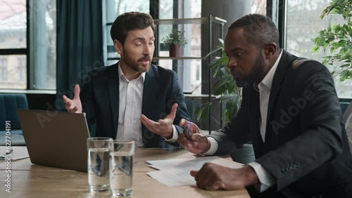 Caucasian businessman insurance agent consult African American male client advise financial offers showing presentation on laptop. Two diverse businessmen men at office discuss project with computer photo