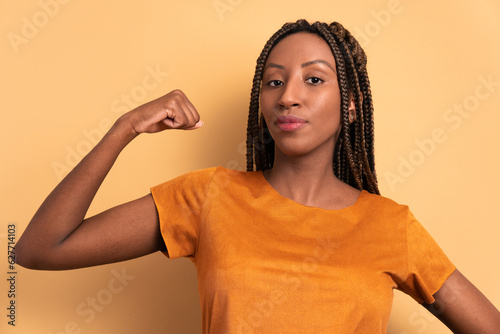 trustworthy black young woman flexing arms in beige colors. strong, power, proud concept. photo