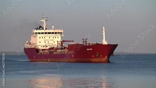 A containerized cargo ship enters the port for unloading. Big container ship entering the industrial port, red colour ultra large empty container ship at sea, top down view. Cargo ship enters port