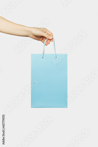 female hand holds a small blue shopping bag isolated on gray background. sale, shopping concept