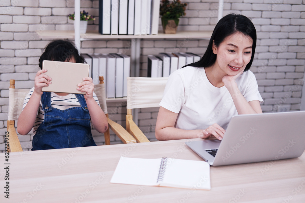 Smiling Asian mother and little girl child is learning by tablet and online learning with laptop together in living room. Homeschool and educational with technology concept. Smiling Asian mother and little girl child is learning by tablet and online learning with laptop together in living room. Homeschool and educational with technology concept.