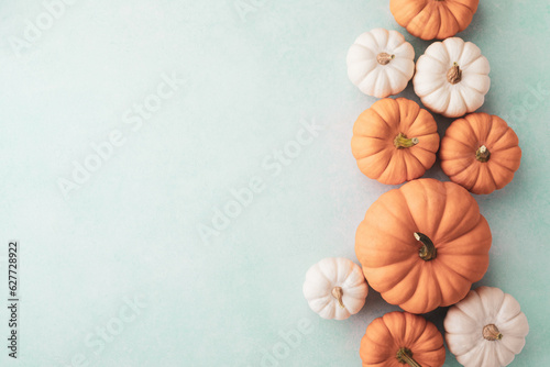 Border of small decorative pumpkins on blue background top view, flat lay. Autumn, Thanksgiving or Halloween minimalist greeting card