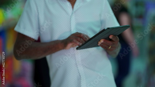 Close-up of a senior black man hands holding tablet device. Elderly person hand detail engaged with modern technology