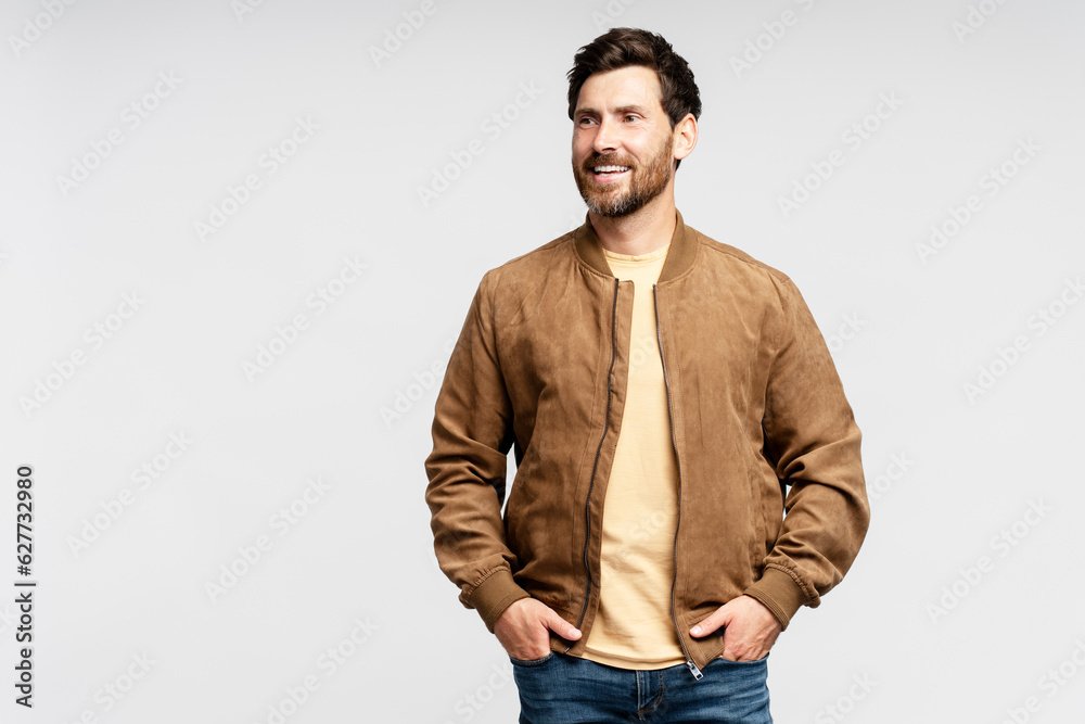 Handsome smiling bearded man wearing brown autumn jacket, stylish jeans isolated on gray background. Portrait of successful middle aged fashion model posing for pictures, studio shot Handsome smiling bearded man wearing brown autumn jacket, stylish jeans isolated on gray background. Portrait of successful middle aged fashion model posing for pictures, studio shot