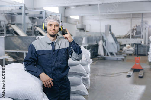 Industrial man loader in uniform holding trolley with bags of coffee beans or wheat, nuts in warehouse of manufacturing factory