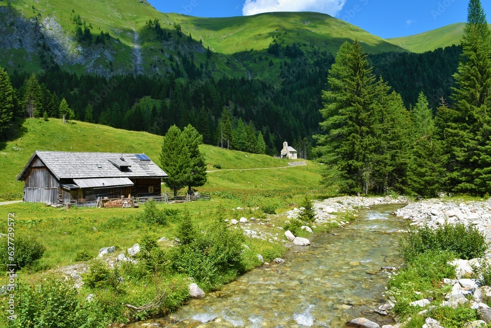Obraz premium Muritzen stream and a alpine pasture with a wooden lodge and a chapel behind and mountain above at Hintermuhr, Austria