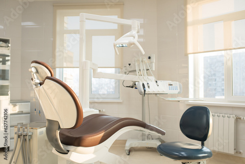 Nobody in clean modern dentists office: leather dental chair and operator stool, dental operating light, dental equipments for treatment