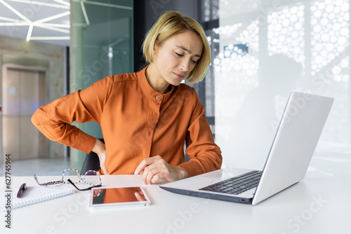 Papier peint Tired and overworked woman working at workplace inside office, business woman has severe back pain, upset blonde massaging muscle, long sitting work
