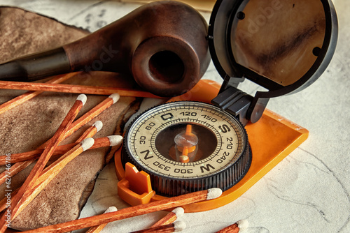 Old orange compass, smoking pipe and matches on the table. Vintage adventure equipment. Pirates theme