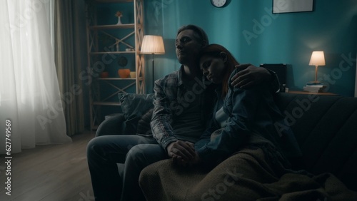 A couple is sitting on a sofa in a dark room close up. A man holds a woman by the hand, hugs. Support for the couple, joint problem solving, reconciliation and understanding in relationships.
