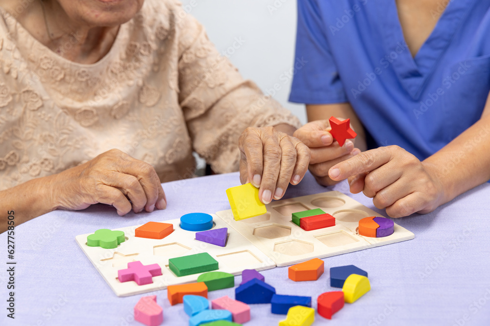 Caregiver and senior woman playing wooden shape puzzles game for dementia prevention Caregiver and senior woman playing wooden shape puzzles game for dementia prevention