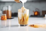 Pouring milk into a glass with warm coffee drink with pumpkin spice or cinnamon, whipped milk foam and chocolate in a white sunlit modern kitchen interior. Generative AI technology