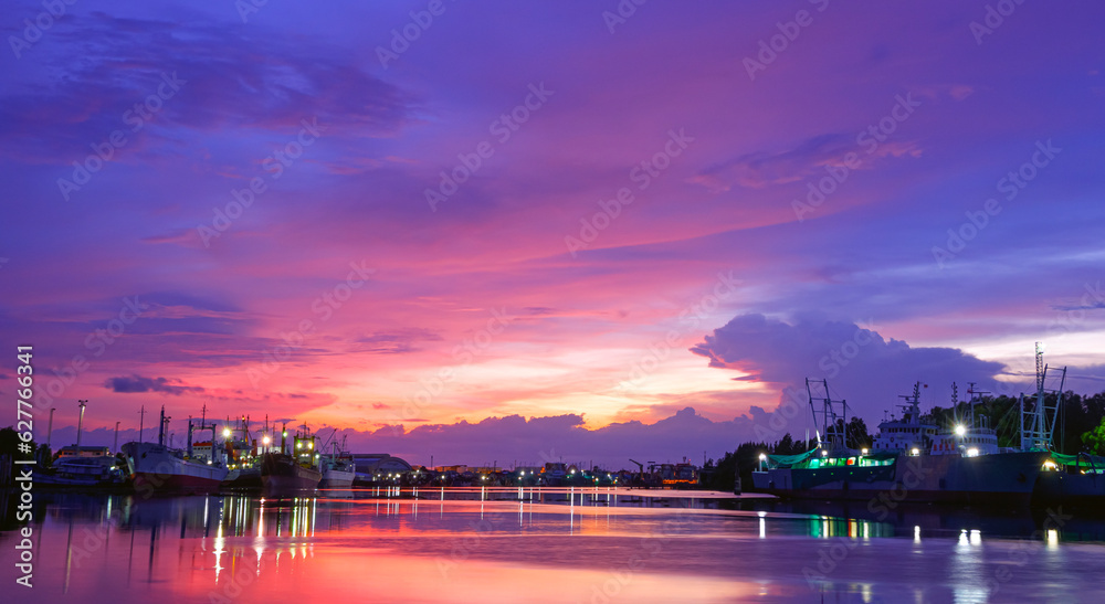 Beautiful orange sunlight clouds on colorful dramatic sunset sky over riverbank with nautical vessels moored along the coast