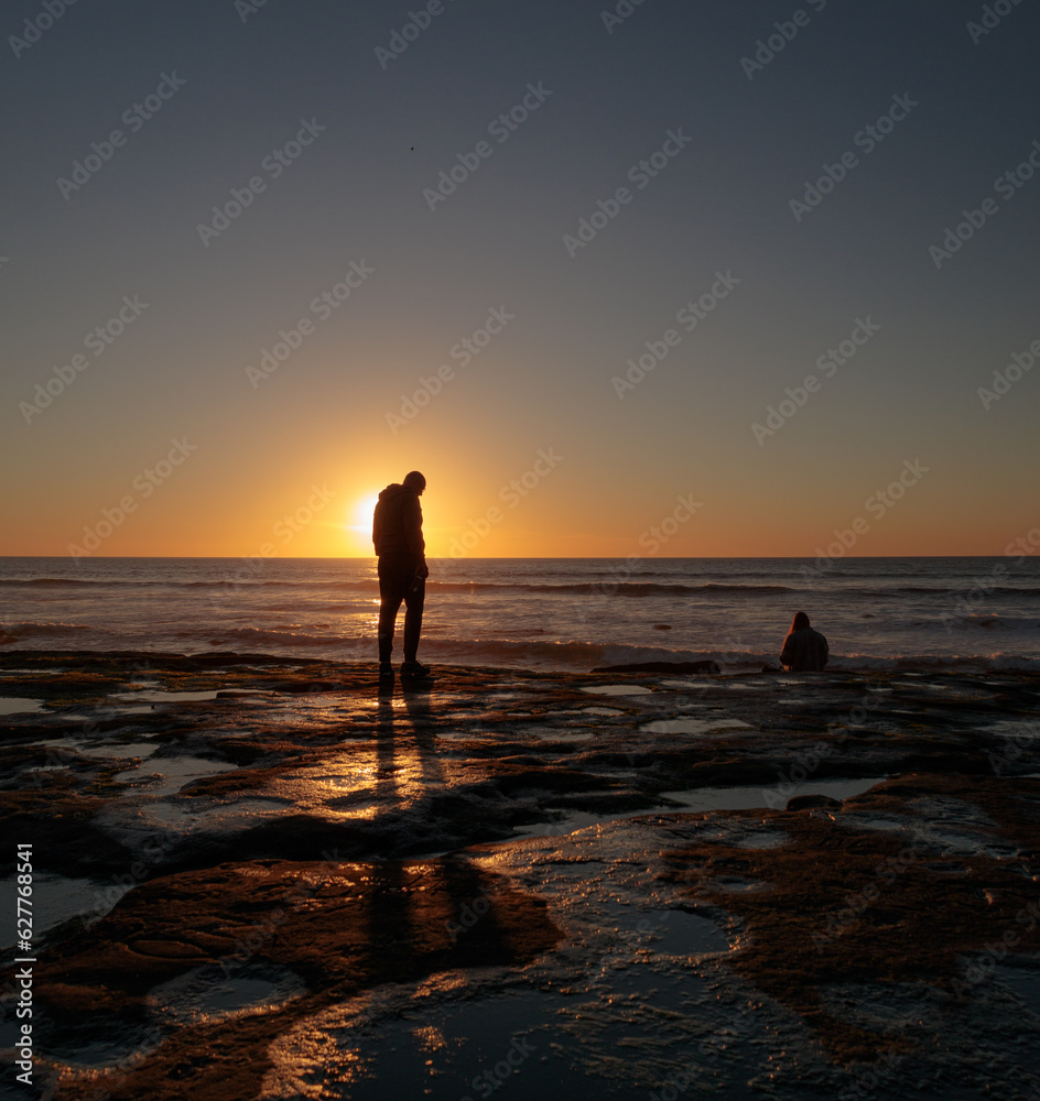 Person standing in front of Sunset over tidepools at beach in San Diego California